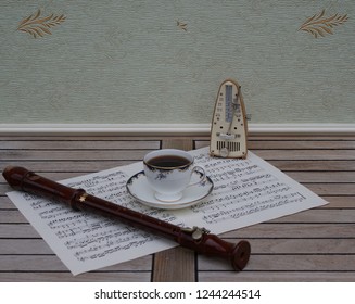 English Teacup With Saucer, Fine Bone China Porcelain, Metronome For Music And A Block Flute On A Sheet Of Music