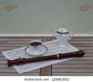 English Teacup With Saucer And Sugar Bowl, Fine Bone China Porcelain, And A Block Flute On A Sheet Of Music