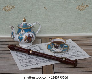 English Teacup With Saucer And Teapot, Fine Bone China Porcelain, And A Block Flute On A Sheet Of Music