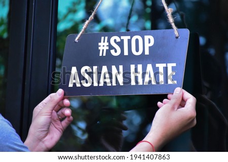 English texts ‘#Stop Asian Hate’ on label holding in hands in front of the glass door, concept for calling to stop hurting and hating Asian people around the world. Selective on English texts.