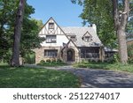 English Tudor-style, stucco and stone house with slate roof and mature trees.