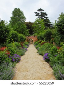 An English Walled Garden In Early Summer With Path Leading To An Arched Gate