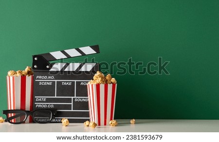 Enhance your film's launch with tasty treat concept. Side view photo featuring table adorned with producer's movie clapper, 3D glasses, popcorn on green wall background, room for movie promotion Stockfoto © 
