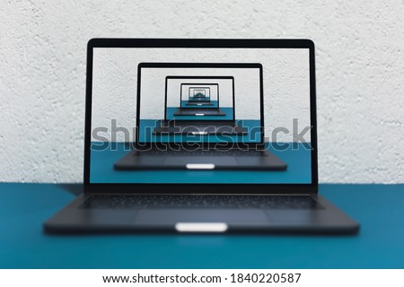 Enigmatic surrealistic optical illusion. Close-up of modern laptop on blue table, background of grey textured wall.