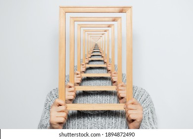 Enigmatic surrealistic optical illusion, young man holding frame on grey background.