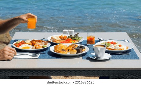 Enjoy a delicious breakfast at a tropical hotel resort. Man drinking orange juice on buffet breakfast at a luxurious beachfront villa. Dining at a beachside restaurant - Powered by Shutterstock