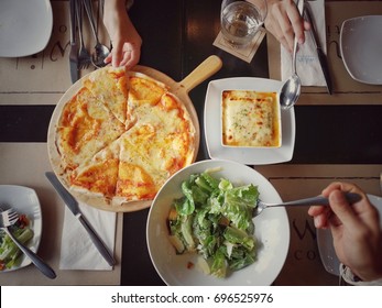 Enjoy Eating Family Meals With Hands Taking Food Italian Pasta, Pizza, Lasagna And Caesar Salad In Vintage Style Restaurant Top View.  