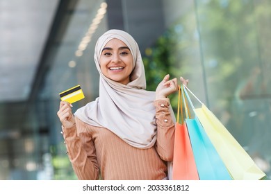 Enjoy Great Shopping After Covid-19 Quarantine, Fast Checkout. Portrait Of Satisfied Young Cute Middle Eastern Woman In Hijab With Color Purchases Bags And Credit Card Near Mall Outdoor, Copy Space