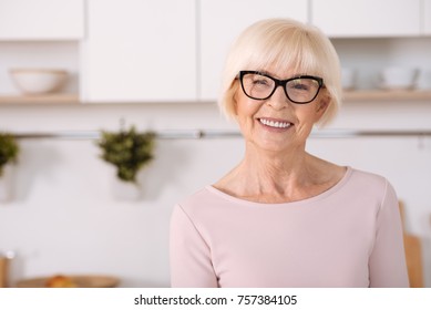 Enjoy Home Atmosphere. Nice Cheerful Aged Woman Smiling And Standing In The Kitchen