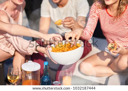 Enjoy it. Close up of bowl with snacks in hands of a young woman holding it while sharing with her friends