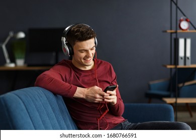 Enjoy listening to music.Young man in headphones listening music on smart phone using music app. Portrait of guy in earphones and mobile phone at home. Relaxation, leisure and stress management.