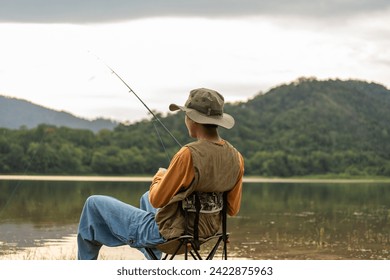 Enjoy moment of Handsome man fishing as a leisure activity during his vacation at the lake on sunset. Silhouette at sunset moment of man fishing rotation with reel. - Powered by Shutterstock