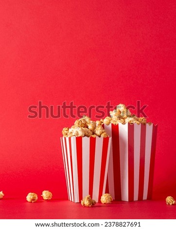 Enjoy movie nights with friends and tasty treats. Side vertical view image of a table featuring delectable popcorn in striped boxes against a red wall backdrop, perfect for film promotions Stockfoto © 