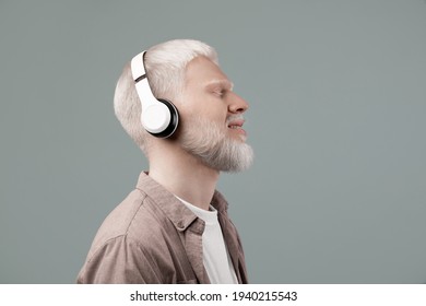 Enjoy the sound. Peaceful albino guy listening to music with closed eyes in wireless headset, enjoying melodies over grey background - Powered by Shutterstock