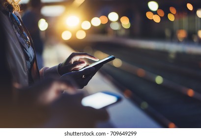 Enjoy travel. Young woman wait on station platform on background light electric moving train using smart phone in night. Tourist text message and plan route of stop railway, railroad transport