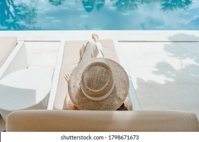 Enjoy vacations in luxury hotel with swimming pool. Relaxing young caucasian beautiful female resting in vacation on summer season with hat at resort swimming pool edge with chair beach on side