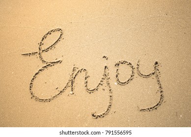 Enjoy word is written on the beach sand