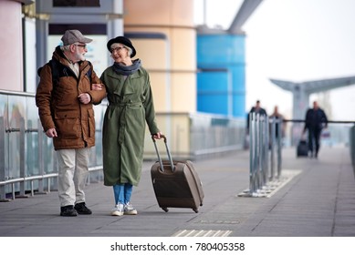 Enjoy your life. Full length of encouraged calm retired man and woman are talking to each other while standing outdoors. They are carrying suitcase while looking at each other with love. Copy space