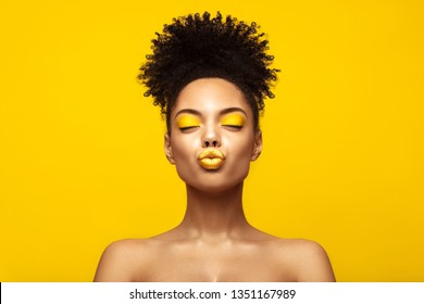 Enjoyed African American Fashion Model portrait . Satisfied Brunette young woman with afro hair style and closed eyes show kiss, creative yellow make up, lips and eyeshadows on colorful background.