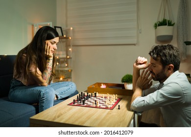 Enjoying A Board Game. Focused Young Wife And Handsome Husband Playing A Match Of Chess During A Date Night At Home