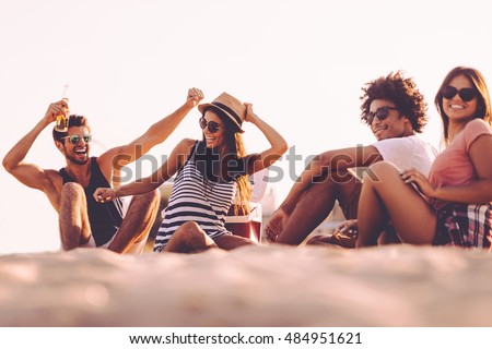 Enjoying carefree time with friends. Cheerful young people spending nice time together while sitting on the beach and drinking beer