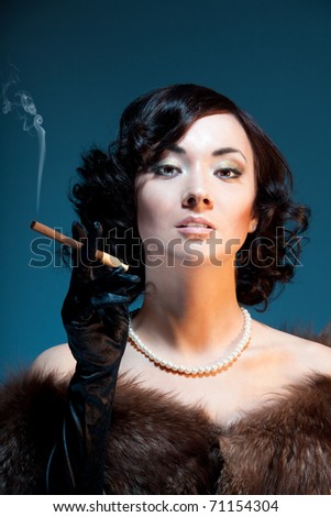 Enjoying cigar - woman standing and smoking cigar on blue background