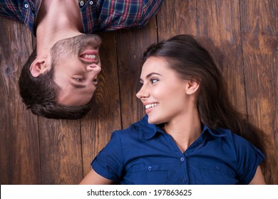 Enjoying closeness. Top view of beautiful young loving couple lying together on the hardwood floor and looking at each other 