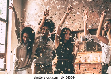 Enjoying cool party. Group of happy young people throwing confetti and jumping while enjoying home party on the kitchen - Shutterstock ID 1043488444