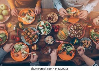 Enjoying dinner with friends. Top view of group of people having dinner together while sitting at the rustic wooden table