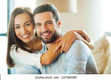 Enjoying every minute together. Beautiful young loving couple sitting together on the couch while woman embracing her boyfriend and smiling  - Shutterstock ID 237584389