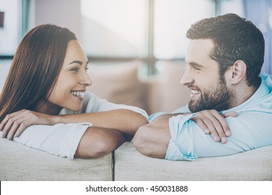 Enjoying every moment together. Beautiful young loving couple sitting together on the couch and looking at each other with smile