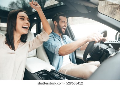 Enjoying fun travel. Beautiful young couple sitting on the front passenger seats and laughing while handsome man driving a car