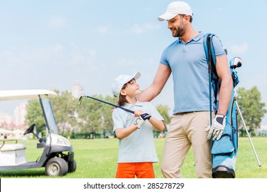 Enjoying great game together. Smiling young man and his son looking at each other while standing on the golf course
