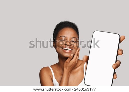 Enjoying healthy woman holding smartphone with white empty blank screen display on gray studio wall background. Happy model with phone