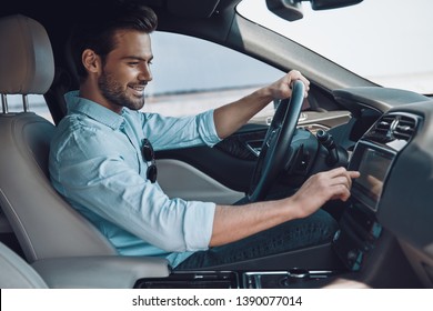 Enjoying His Drive. Handsome Young Man In Smart Casual Wear Smiling While Driving A Status Car