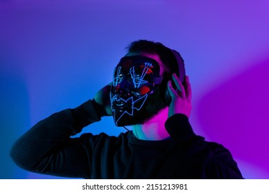 Enjoying His Favorite Music. Man In Mask With Headphones Listening While Standing Against Blue Neon Background