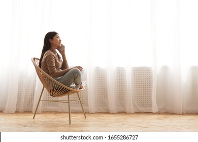 Enjoying home comfort. Girl talking on phone in cozy chair against window, side view with copy space - Shutterstock ID 1655286727