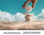 Enjoying Life Concept. Harmony and Positive Mind. Hand Setting Natural Pebble Stone with Smiling Face Cartoon to Balance on Beach Sand. Balancing Body, Mind, Soul and Spirit. Mental Health Practice