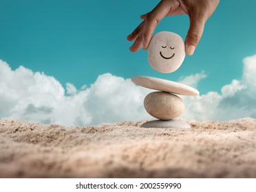 Enjoying Life Concept. Harmony and Positive Mind. Hand Setting Natural Pebble Stone with Smiling Face Cartoon to Balance on Beach Sand. Balancing Body, Mind, Soul and Spirit. Mental Health Practice - Shutterstock ID 2002559990