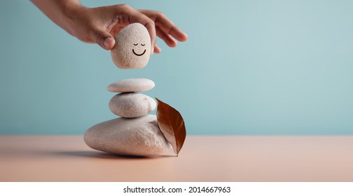 Enjoying Life Concept. Harmony and Positive Mind. Hand Setting Natural Pebble Stone with Smiling Face Cartoon to Balance. Balancing Body, Mind, Soul and Spirit. Mental Health Practice
