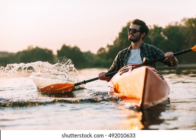 Enjoying life on river. Handsome young smiling man splashing water while kayaking on river