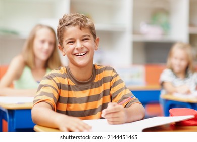 Enjoying a lighthearted moment in class. Sweet schoolboy sitting at his desk in class laughing happily. - Shutterstock ID 2144451465