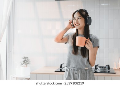 Enjoying moment of relaxation, young woman in cozy kitchen wears headphones while holding cup. Her cheerful expression reflects sense of comfort and joy. - Powered by Shutterstock