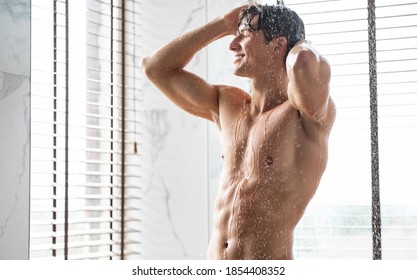 Enjoying The Morning. Portrait Of Handsome Muscular Man Taking A Shower Washing Head Standing Under Falling Hot Water In Modern Bathroom At Home. Male Bodycare Beauty Routine And Everyday Hygiene