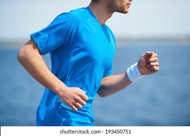 Enjoying A Morning Run.  Side View Of Young Man Running Along The Riverbank 