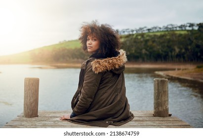 Enjoying Natures Quiet. Portrait Of A Young Woman Looking Over Her Shoulder While Sitting On A Pier.