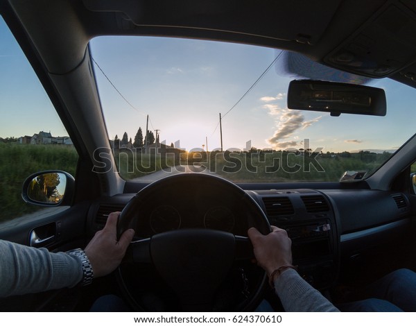 Enjoying a nice road trip at sunset. Young\
adult man driving a car. Personal\
perspective.