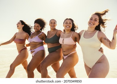 Enjoying our beach day together. Happy young women embracing each other while wearing swimwear at the beach. Carefree female friends having fun and enjoying their summer vacation.