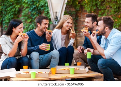 Enjoying Pizza Together. Group Of Happy Young People Eating Pizza While Sitting Outdoors