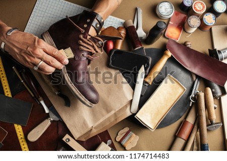 Enjoying process of creation custom made shoes. Workplace of shoe designer. Hands of shoemaker dealing with cobbler tool, close up